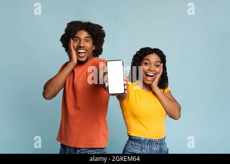 Un couple afro-américain émerveillé montrant un smartphone avec écran vide, maquette Banque D'Images