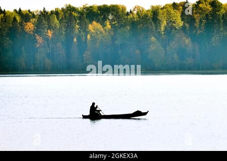 Waterman. Old Veps se déplace à travers le lac en bateau de bois de fortune, brouillard léger. Lac forestier dans les tons jaunes d'automne. Silhouette anonyme méconnue Banque D'Images