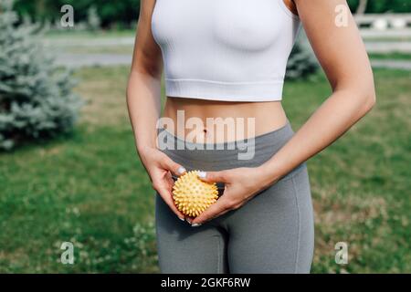 gros plan d'une balle de massage à pointes dans les mains d'une femme sur la pelouse dans le parc, équipement pour se détendre dans le yoga ou le pilatos Banque D'Images