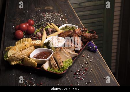 Assortiment de viande d'ailes de poulet frites, de bœuf et de porc décorées de laitue et de tomates cerises Banque D'Images