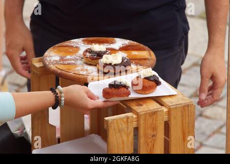 Un vendeur dans un stand sur le marché alimentaire de rue des agriculteurs de Naulavka offre aux clients des beignets bavarois, des beignets frits en pâte de levure à la prune Banque D'Images