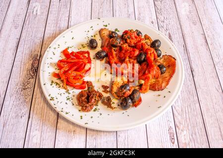 Escalopes de porc recette avec tomates déshydratées, poivrons piquillo, olives noires et origan sur une assiette blanche Banque D'Images