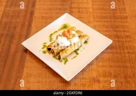 Tacos d'or ou flautes mexicaines avec tortilla au maïs poêlée farcies aux haricots avec fromage à la crème et pico de gallo avec huile verte et sauce au persil Banque D'Images