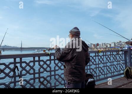 Eminonu, Istanbul, Turquie - 04.13.2021: Un homme d'âge moyen utilise une barre de pêche en fer près de la clôture d'un pont et attend les poissons autour du pont de Galata Banque D'Images