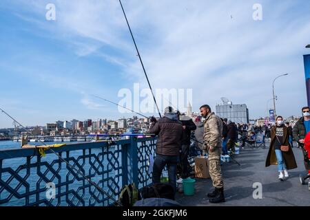 Eminonu, Istanbul, Turquie - 04.13.2021: Plusieurs pêcheurs avec des masques protecteurs parlant et pêchant avec des barres de pêche en fer près de la clôture d'un pont et W Banque D'Images