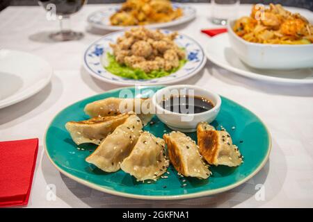 Assiette avec une portion de gyozas cuits sur le grill, dim sum, sauce soja, graines de pavot et sésame sur une assiette bleue d'un restaurant chinois Banque D'Images