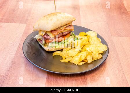 Hamburger de bœuf avec œuf, fromage, bacon et laitue dans un pain rustique et des frites sur une assiette noire Banque D'Images