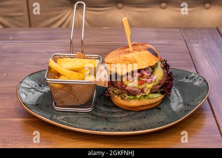 Hamburger mexicain avec 200 grammes de bœuf, guacamole et pico de gallo et garniture de pommes de terre dans une friteuse métallique sur une assiette bleue Banque D'Images