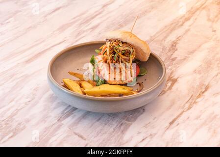 Hamburger de poisson avec taco de saumon norvégien, compote de légumes, laitue tomate et agneau garnie de frites sur un plateau gris et une table en marbre Banque D'Images