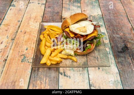 Hamburger de bœuf avec beaucoup de pousses de laitue mélangées, fromage cheddar, œuf frit et beaucoup de bacon sur une assiette de verre Banque D'Images