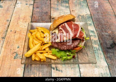 Hamburger de bœuf au fromage fumé et jambon Serrano à la laitue avec une portion de frites sur une assiette en verre transparent Banque D'Images