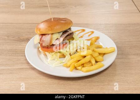 Hamburger de bœuf classique avec bacon, jambon, concombres marinés, tomate et oignon et une petite portion de frites Banque D'Images