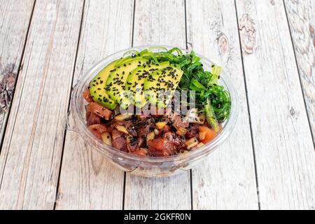 Bol en plastique transparent pour livraison à domicile avec tartare de thon rouge, graines de pavot noir, algues wakame avec gouacamole tranché et riz blanc Banque D'Images