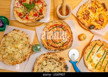 Vue de dessus : pizzas délicieuses et originales avec poire, champignons, sauce au pesto, asperges vertes et œufs frits sur une table en bois de pin Banque D'Images