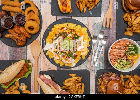 Prise de vue en hauteur de plats de restauration rapide, hors-d'œuvre classiques, cuisine tex mex et au centre une assiette de nachos avec guacamole sur une table en bois Banque D'Images