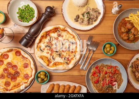 Ensemble de pâtes et de plats espagnols sur une table en bois. Croquettes, petits pois au jambon, pain de bœuf en sauce, pizza au pepperoni, nouilles sautées. Poulet ste Banque D'Images