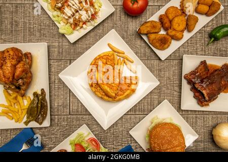 Ensemble de assiettes à nourriture pour le dimanche. Hamburgers, omelette aux pommes de terre, salade césar, croquettes et hors-d'œuvre, poulet entier rôti aux poivrons et aux frites, côtes grillées Banque D'Images