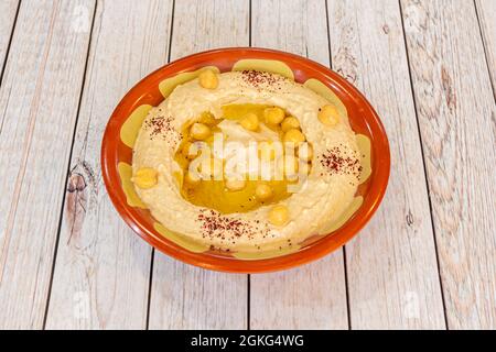 Houmous de pois chiches cuits à l'huile d'olive vierge, grains de paprika dans un bol en argile sur une table en bois clair Banque D'Images