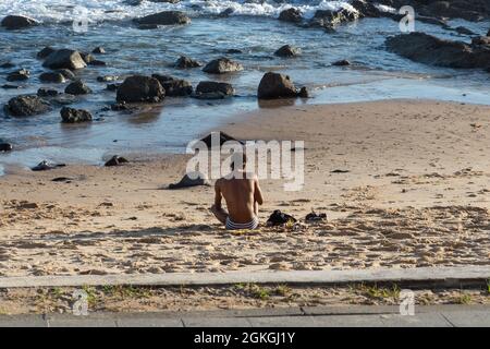 Salvador, Bahia, Brésil - 17 juin 2021: Homme assis sur le sable de Porto da Barra plage appréciant la nature. Banque D'Images