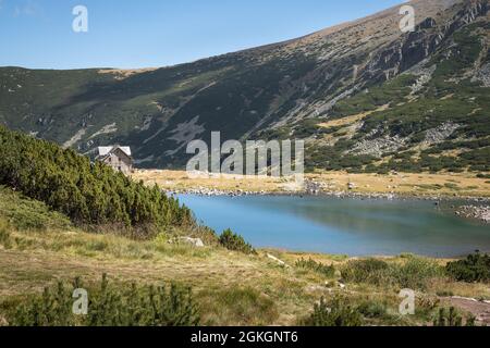 Vif, bleu, lac glaciaire et une cabane de montagne sur la montagne de Rila, sur la piste du sommet de Musala, sous un ciel clair et bleu Banque D'Images