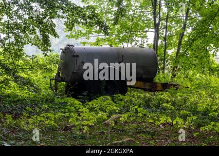 Un vieux épandeur de fumier rouillé est abandonné au milieu de la verdure Banque D'Images