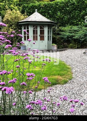Une maison d'été en bois pittoresque dans un jardin de campagne anglais avec de l'herbe verte et des fleurs de verveine Banque D'Images