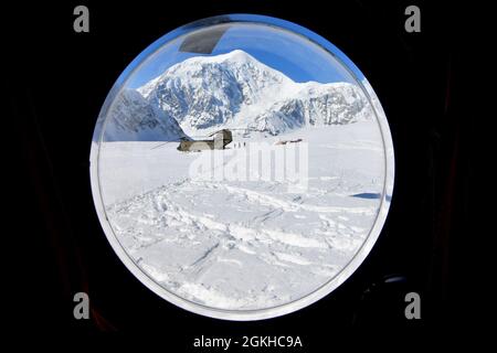 La fenêtre à bulles d'un hélicoptère CH-47F Chinook offre une vue circulaire des soldats de la Compagnie B, du 1er Bataillon, du 52e Régiment d'aviation et d'un autre Chinook sur le glacier Kahiltna, le 22 avril 2021. Les aviateurs de l'unité, également connus sous le nom de Sugar Bears, ont voyagé de fort Wainwright pour aider le Service des parcs nationaux à obtenir l'équipement et les fournitures nécessaires pour le camp de base au niveau de 7,200 pieds du glacier Kahiltna pour la saison d'escalade 2021 sur Denali, La plus haute montagne d'Amérique du Nord. La montagne en arrière-plan est le mont Hunter de 14,573 pieds. (Photo de l'armée/John Pennell) Banque D'Images