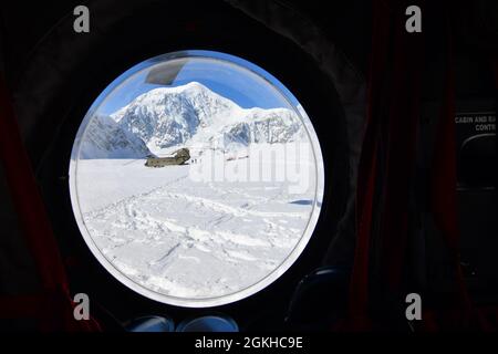 La fenêtre à bulles d'un hélicoptère CH-47F Chinook offre une vue circulaire des soldats de la Compagnie B, du 1er Bataillon, du 52e Régiment d'aviation et d'un autre Chinook sur le glacier Kahiltna, le 22 avril 2021. Les aviateurs de l'unité, également connus sous le nom de Sugar Bears, ont voyagé de fort Wainwright pour aider le Service des parcs nationaux à obtenir l'équipement et les fournitures nécessaires pour le camp de base au niveau de 7,200 pieds du glacier Kahiltna pour la saison d'escalade 2021 sur Denali, La plus haute montagne d'Amérique du Nord. La montagne en arrière-plan est le mont Hunter de 14,573 pieds. (Photo de l'armée/John Pennell) Banque D'Images