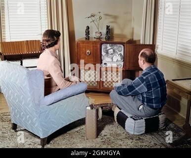 COUPLE D'ÂGE MOYEN DES ANNÉES 1950 MARI ET FEMME ASSIS REGARDANT LA CONSOLE DE TÉLÉVISION NOIR ET BLANC DANS LE SALON - R10114C HAR001 HARS HOMMES ADULTES GRANDS-UP TÉLÉVISION CONSOLE DE DIVERTISSEMENT RÊVES ST LOISIR SALON EXCITATION ÉCHAPPER OTTOMANE VUE ARRIÈRE COMMUNIQUER COMMUNICATIONS HOMME MOYEN-ADULTE FEMME MOYENNE-ADULTE COMBINAISON ORIGINE CAUCASIENNE HAR001 VIEILLES ÉPOUSES Banque D'Images