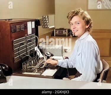 FEMME SOURIANTE DES ANNÉES 1950 BUREAU TÉLÉPHONE STANDARDISTE RÉCEPTIONNISTE REGARDANT L'APPAREIL PHOTO - T2031C HAR001 PORTRAITS HARS GROGNUP COMMUNIQUANT L'ESPACE DE COPIE DEMI-LONGUEUR DAMES PERSONNES ADULTES PROFESSION PANNEAU CONTACT VISUEL STANDARD COMPÉTENCE PROFESSION BONHEUR OPÉRATEUR GAI SERVICE CLIENTÈLE RÉSEAUTAGE CARRIÈRES EMPLOI OCCUPATIONS TÉLÉPHONES SOURIRES CONNEXION TÉLÉPHONES AMICAL JOYEUX EMPLOYÉ AGRÉABLE COMMUNIQUER JEUNES ADULTES FEMME CAUCASIEN ETHNICITÉ HAR001 ANCIEN MODE Banque D'Images