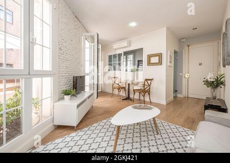 Belle salle de séjour avec mur de briques blanches et de grandes fenêtres menant à la terrasse d'un appartement de grand standing dans un appartement de location de vacances Banque D'Images