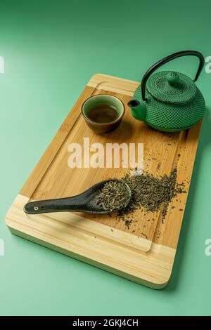 Service de thé vert oriental avec cuillère remplie dans la première assiette sur table en bambou et fond vert Banque D'Images