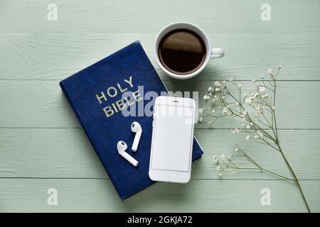 Sainte Bible, écouteurs, téléphone mobile, fleurs de gitsophila et tasse de café sur fond de bois de couleur Banque D'Images