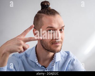 White Young Hipster Man semble heureux et confiant. Il fait le signe de la paix avec ses doigts Banque D'Images