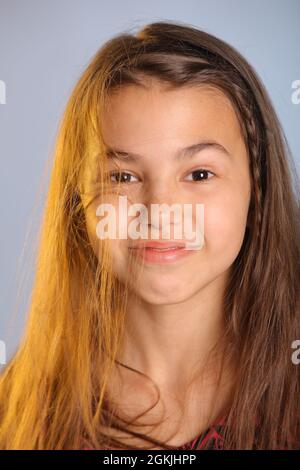 Portrait en gros plan d'une jeune fille adolescente aux cheveux sombres et aux couleurs vives, âgée de 12 ans, vêtu d'une robe mauve, ses yeux bruns rient et regardent d'un œil à l'autre. Banque D'Images