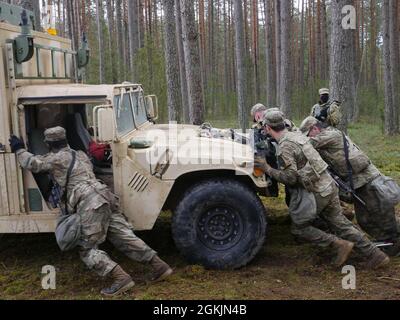 LES soldats AMÉRICAINS de Cavalry du 2e Bataillon, du 8e Régiment de Cavalry, de l’équipe de combat de la 1re Brigade blindée et des forces armées lituaniennes travaillent ensemble pour pousser un véhicule militaire à 150 mètres sur une route sur la voie 3, après avoir réparé un pneu endommagé à Pabrade, Lituanie, le 8 mai 2021. Les troupes AMÉRICAINES et les soldats partenaires de l'OTAN ont travaillé en équipe tout au long de l'événement Spur Ride de 40 heures pour gagner leurs éperons. L'événement a été l'occasion de faire l'expérience de différents styles de leadership dans un environnement tactique à l'échelle multinationale. Banque D'Images