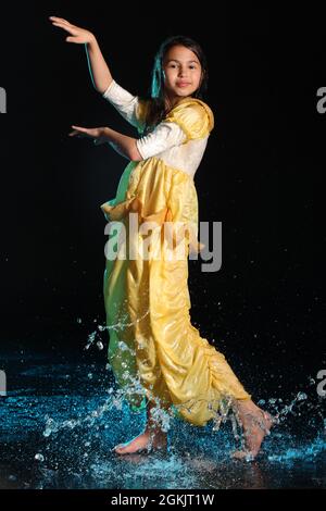 Brillant mince belle et gaie à cheveux foncés adolescente 12 ans dans une robe de soie jaune pieds nus dans un aquazone noir. Émotions et danse Banque D'Images