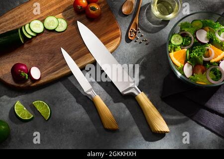 Table de découpe et couteaux de cuisine avec légumes frais sur table grise. Concept de saine alimentation. Banque D'Images