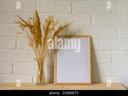 Une maquette d'un cadre photo vide et d'un bouquet d'automne d'herbes séchées dans un vase transparent sur une table en bois avec une copie de l'espace Banque D'Images