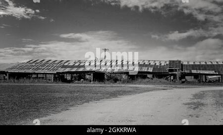 Noir et blanc d'un long bas hangar vieux décrépite avec toit en fer rouillé sur un fond ciel nuageux Banque D'Images