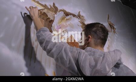 Un artiste designer dessine un aigle sur le mur.Artisan décorateur peint une image avec de l'huile acrylique couleur.Peintre peintre vêtu d'un manteau de peinture. Banque D'Images