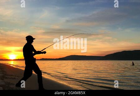 Un jeune homme pêche sur un lac au coucher du soleil Banque D'Images