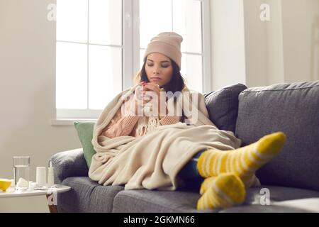Jeune femme malade souffrant de mauvais rhume ou de grippe, assis enveloppé dans une couverture, et boire du thé chaud Banque D'Images
