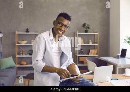 Portrait d'un homme afro-américain confiant et heureux dans son bureau à domicile confortable et élégant. Banque D'Images