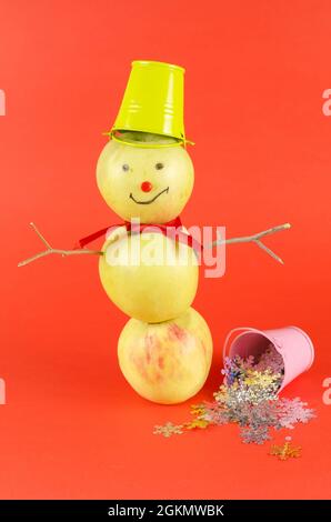 Bonhomme de neige aux pommes avec un seau vert sur sa tête debout sur un rouge Banque D'Images