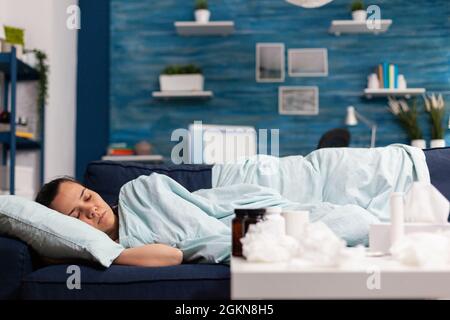 Femme malade dormant à la maison sur le canapé, se rétablissant après les symptômes du rhume et de la grippe. Avoir de la fièvre et prendre un traitement médical tout en se reposant dans la chambre à coucher après la maladie saisonnière Banque D'Images
