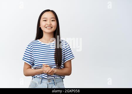 Souriant asiatique fille a l'air poli et professionnel, prêt à aider et à fournir de l'aide, se tient contre fond blanc Banque D'Images