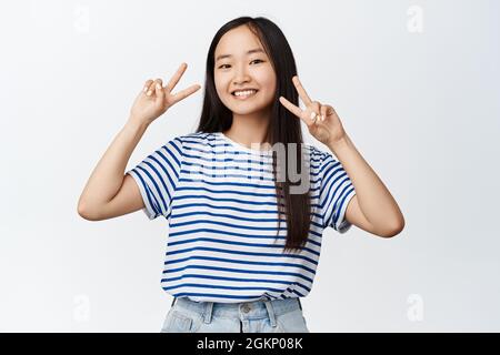 Style de vie et personnes. La jeune femme brune montre des signes de la paix et sourit à la caméra, se tient sur fond blanc Banque D'Images