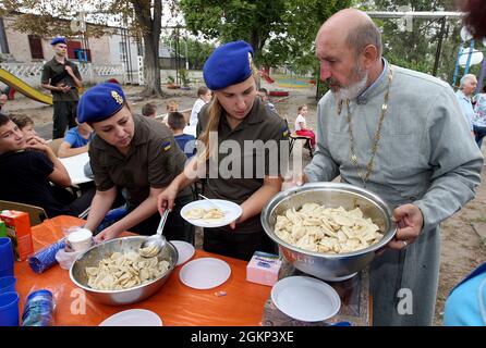 DNIPRO, UKRAINE - le 14 SEPTEMBRE 2021 - Un prêtre et des soldats de la Garde nationale d'Ukraine ont mis des boulettes sur les plaques lors de l'événement caritatif ukrainien Dumpling Holiday organisé par l'équipe de la Fondation Real Dreams Charitable, Dnipro, dans l'est de l'Ukraine Banque D'Images