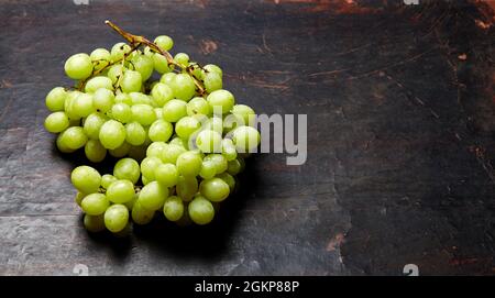 Branche de raisin vert mûr avec gouttes d'eau. Raisins juteux sur fond de bois, gros plan. Raisin sur table de cuisine sombre avec espace pour copier Banque D'Images